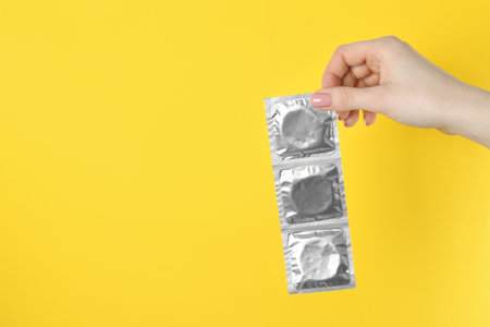 Woman holding condoms on yellow background, closeup. Space for textの写真素材