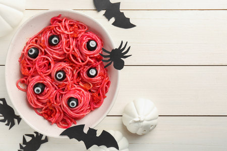 Red pasta with decorative eyes and olives in bowl on white wooden table, flat lay with space for text. Halloween foodの写真素材