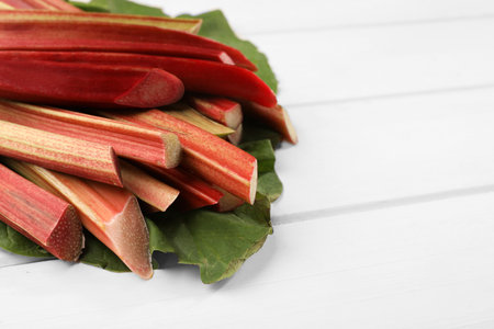 Many cut rhubarb stalks and leaves on white wooden table, closeup. Space for textの写真素材