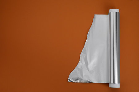 One roll of aluminum foil on brown background, top view. Space for textの写真素材
