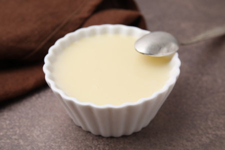 Bowl with condensed milk and spoon on brown table, closeup