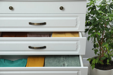 Sorting and organizing. Chest of drawers with different folded clothes indoors