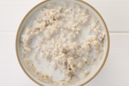 Tasty boiled oatmeal in bowl on white wooden table, top viewの写真素材