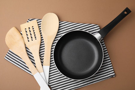 Different kitchen utensils, napkin and frying pan on light brown background, flat layの写真素材