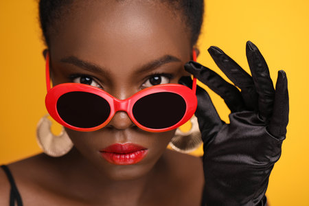 Fashionable portrait of beautiful woman with stylish sunglasses on yellow background, closeupの写真素材