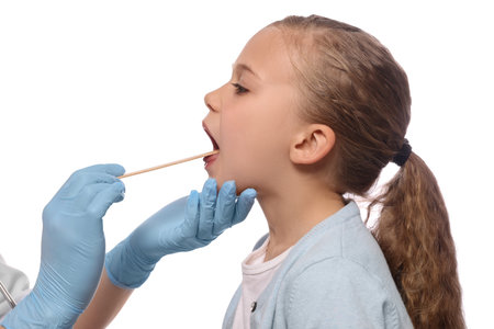 Doctor examining girl`s oral cavity with tongue depressor on white backgroundの写真素材