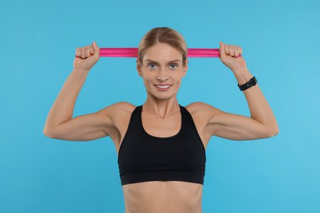 Woman exercising with elastic resistance band on light blue background