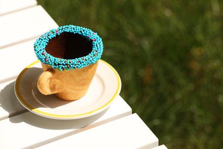 Delicious edible biscuit coffee cup decorated with sprinkles on white wooden table outdoors, space for textの写真素材