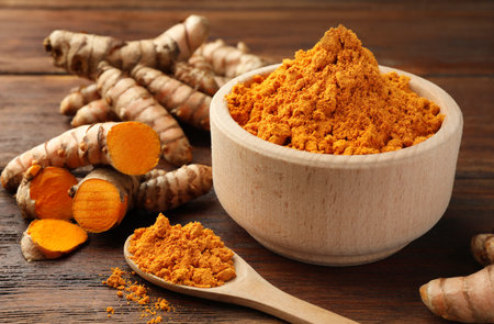 Aromatic turmeric powder and raw roots on wooden table, closeupの写真素材