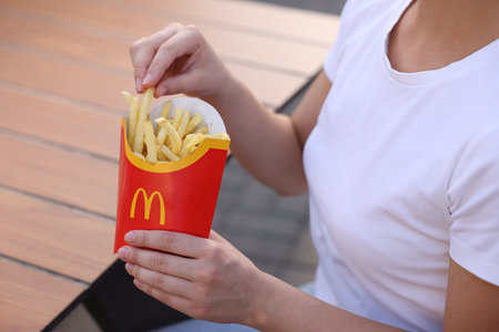 Lviv, Ukraine - September 26, 2023: Woman with McDonald's French fries at wooden table outdoors, closeupのeditorial素材