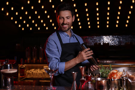 Bartender with shaker preparing fresh alcoholic cocktail in bar