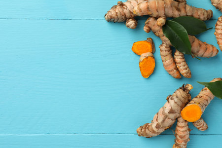 Whole and cut turmeric roots on light blue wooden table, flat lay. Space for text
