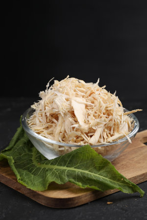Grated horseradish in bowl, leaf and board on black table, closeup. Space for textの写真素材