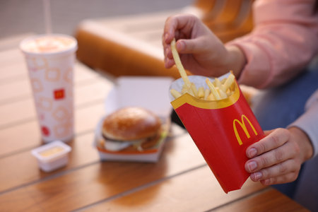 Lviv, Ukraine - September 26, 2023: Woman eating McDonald's menu at wooden table outdoors, closeup