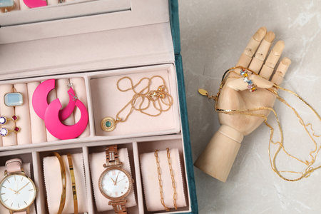 Jewelry box with many different accessories and mannequin hand on light grey table, flat lay