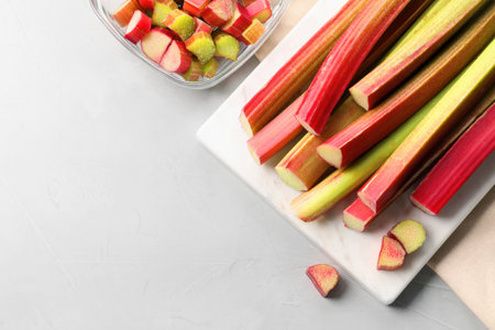 Whole and cut rhubarb stalks on white table, flat lay. Space for text