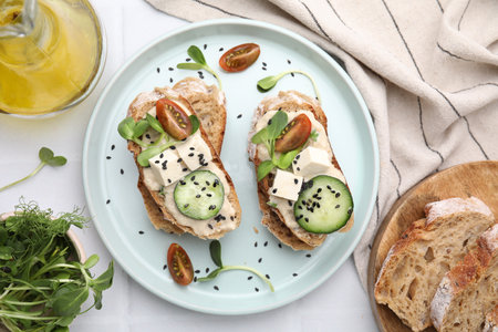 Tasty vegan sandwiches with tofu, cucumber, tomato and sesame seeds on white tiled table, flat lay
