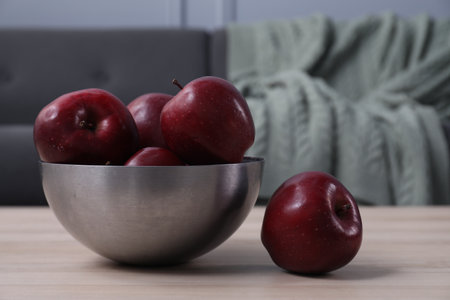 Bowl with red apples on wooden table in room, closeup