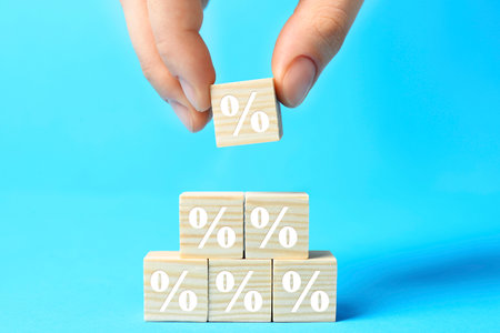 Woman building pyramid of cubes with percent signs on light blue background, closeup