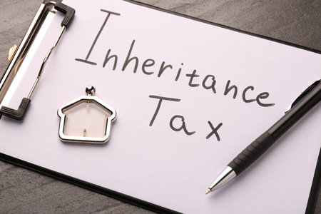 Inheritance Tax. Clipboard, pen and key chain in shape of house on grey table, closeup