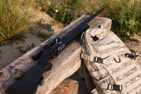 Hunting rifle and backpack on wooden bench outdoors