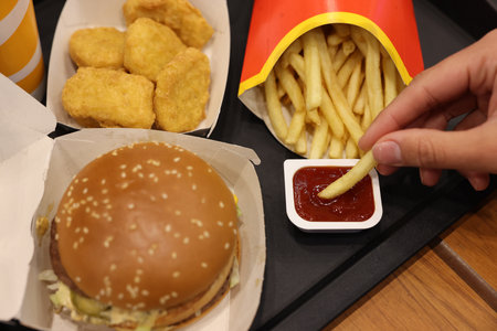 Lviv, Ukraine - October 9, 2023: Woman dipping McDonald's french fry into sauce at wooden table,...