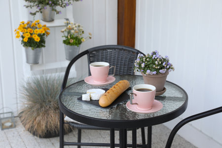 Cups of coffee, potted plant, bread and cheese on glass table. Relaxing place at outdoor terraceの写真素材