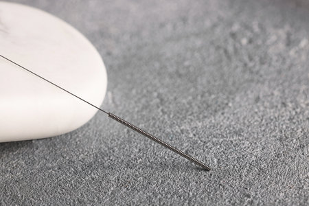 Acupuncture needle and spa stone on grey table, closeup. Space for textの写真素材