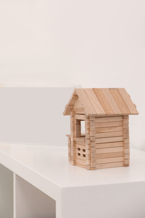 Wooden house on white shelf indoors, space for text. Educational toy for motor skills development