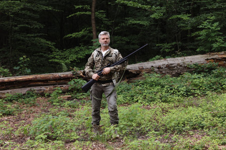 Man with hunting rifle and backpack wearing camouflage in forest