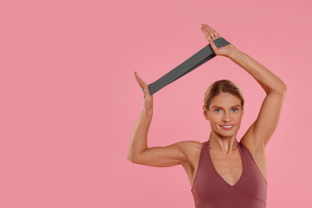 Woman exercising with elastic resistance band on pink background. Space for text