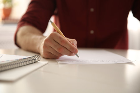Man writing letter at white table in room, closeup
