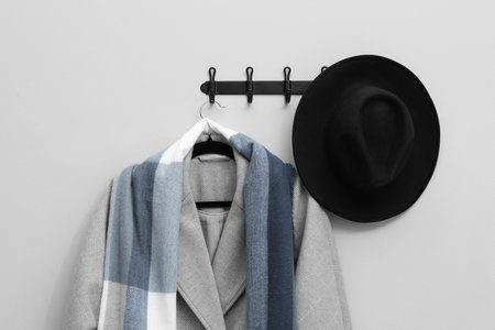 Hanger with coat, scarf and hat on light gray wall