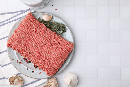 Fresh raw ground meat, peppercorns, garlic and thyme on white tiled table, flat lay. Space for textの写真素材