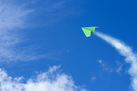Green paper plane flying in blue sky with cloudsの写真素材