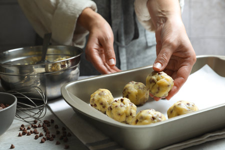 Woman putting raw chocolate chip cookie ball on baking pan at table, closeup