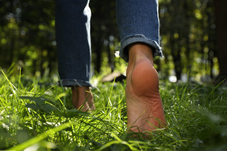 Woman walking barefoot on green grass in park, closeup