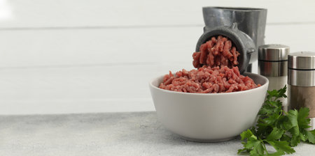 Manual meat grinder with beef mince, spices and parsley on gray table. Banner design with space for...