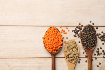 Spoons with different types of lentils on light wooden table, flat lay. Space for text