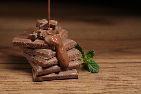Pouring tasty milk chocolate paste onto pieces on wooden table, closeup. Space for text