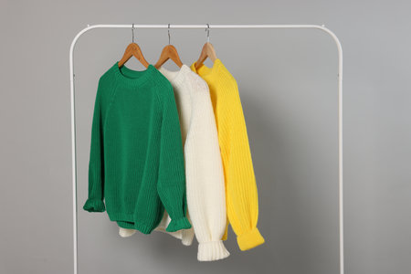 Rack with different warm sweaters on light gray background