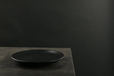 Beautiful ceramic plate on gray table against black background, space for text
