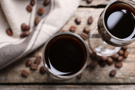 Glasses of coffee liqueur on wooden table, flat lay