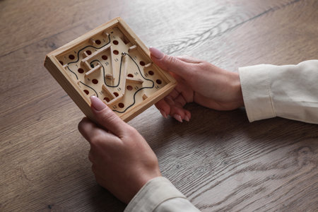 Woman holding wooden toy maze with metal ball at table, closeup