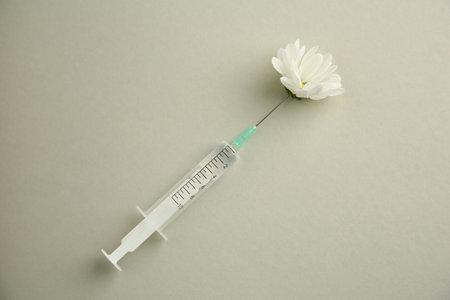 Medical syringe and beautiful chrysanthemum flower on gray background, top view