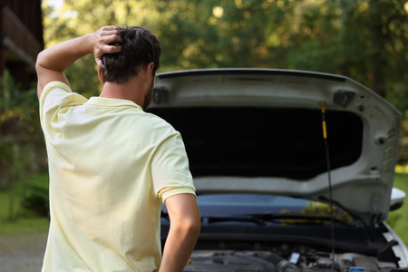 Man looking under the hood of broken car outdoors