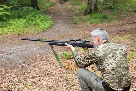 Man wearing camouflage and aiming with hunting rifle in forest