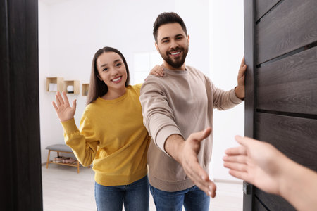 Happy couple welcoming their guest near the door. Invitation to come indoors