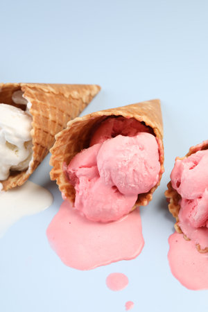 Melted ice cream in wafer cones on light blue background, closeup
