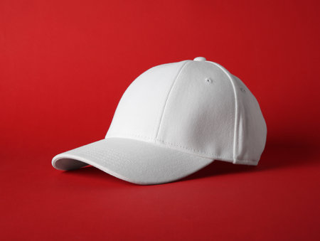 Stylish white baseball cap on red background